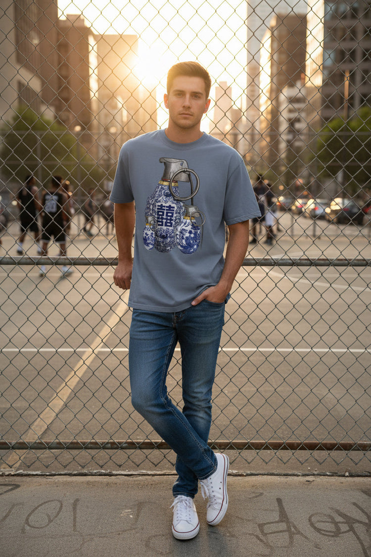 Man in structured fit grenade graphic tee leaning against chain link fence