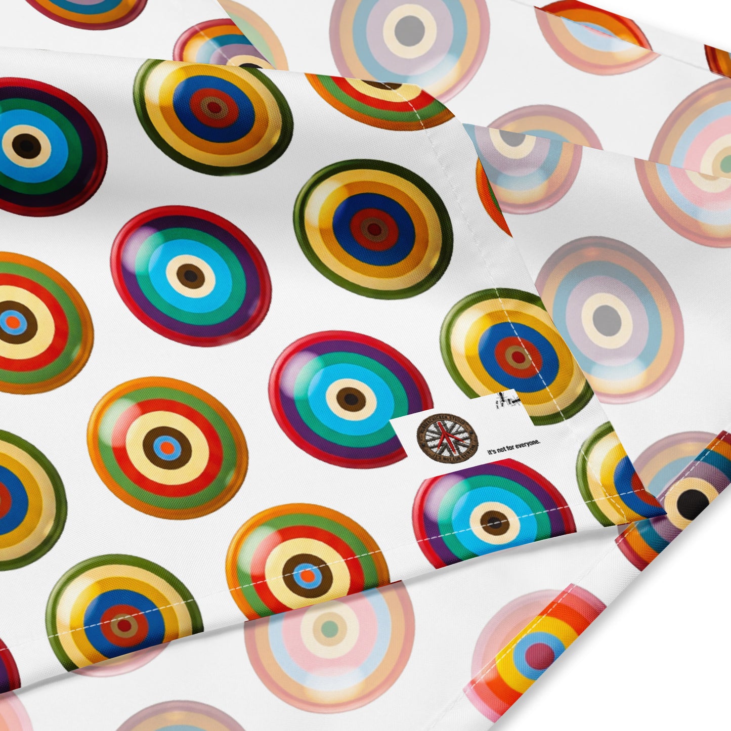 A close-up of bandana featuring a coluorful repeating pattern of concentric target circles. A small fabric tag is visible on the right side.
