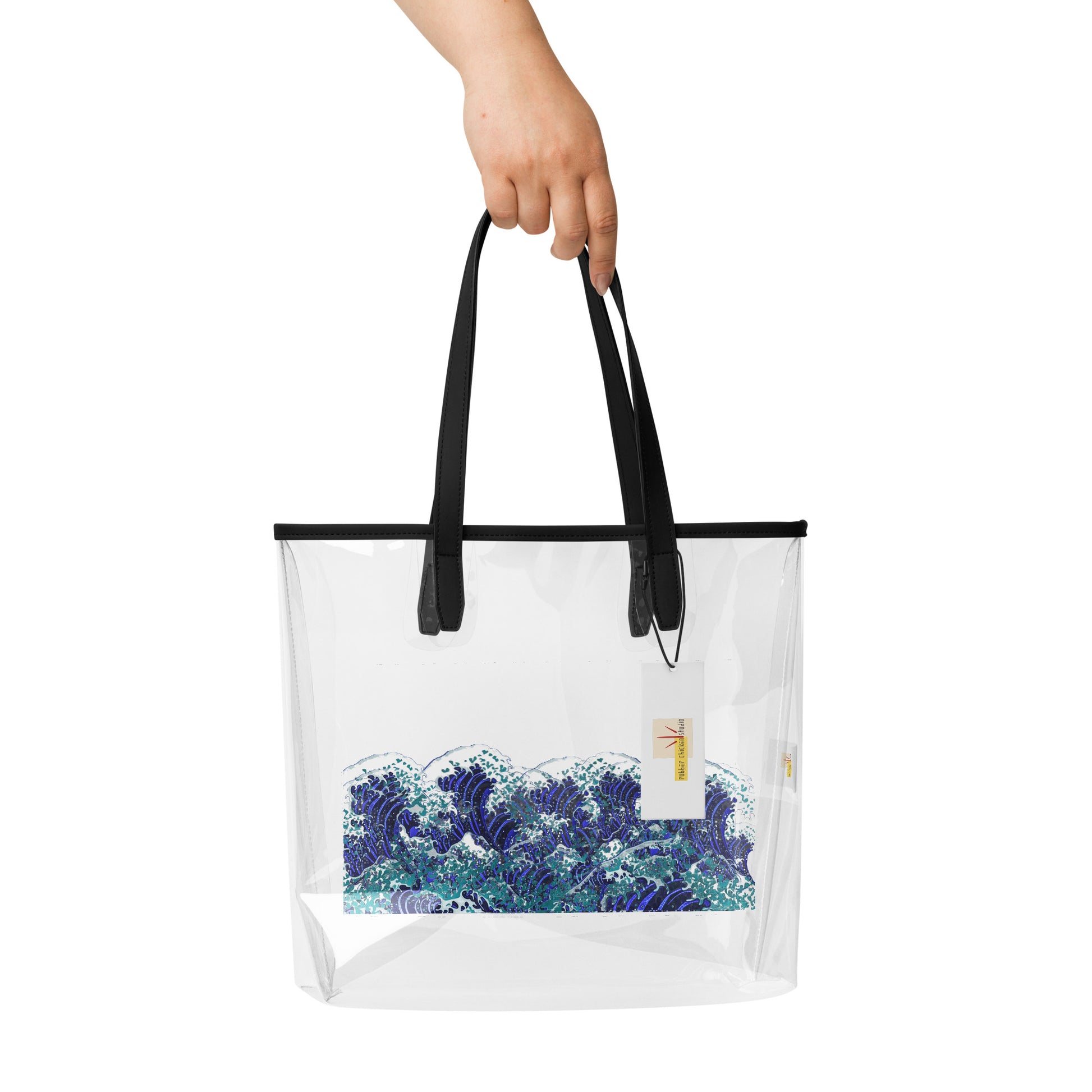 A hand holding a clear plastic tote bag with black handles and a blue and white wave print on the front, shown against a plain white background.